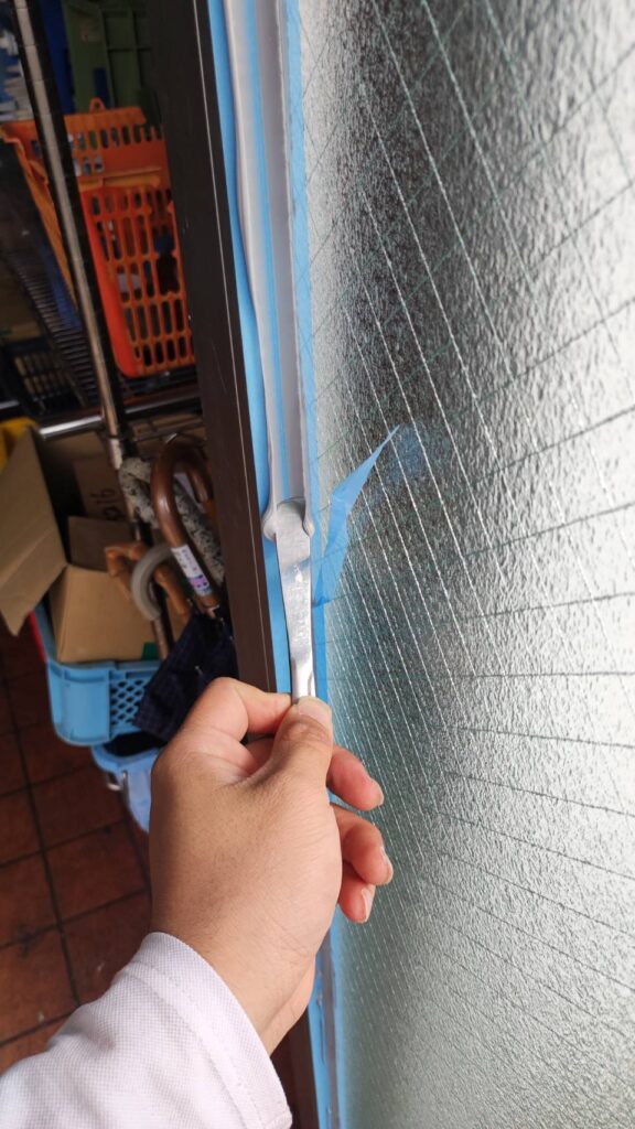 店舗ドアの網入りガラスまわりをコーキングしている様子